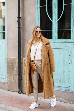 Woman in cream with brown coat smiling outside