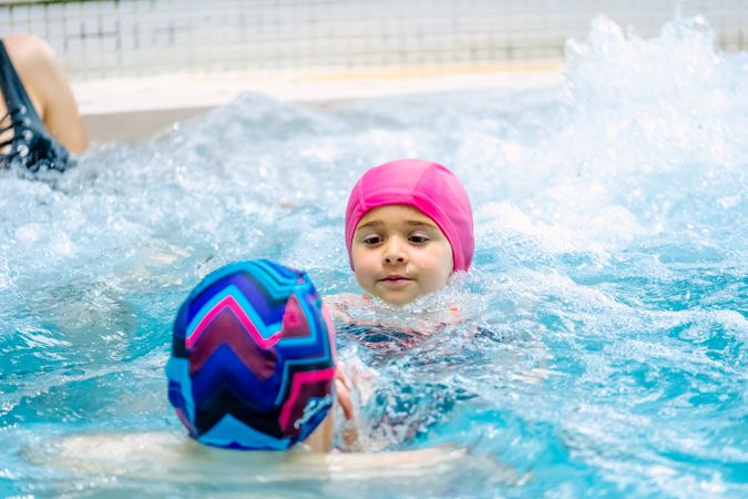 Cheerful girls in hat smiling and swimming in pool in water park