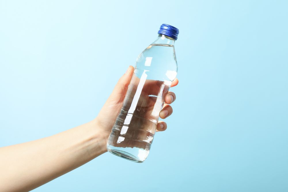 Hand holding plastic water bottle in blue room, copy space