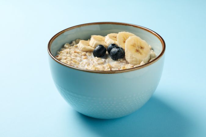 Bowl with oatmeal porridge and fruits on blue background