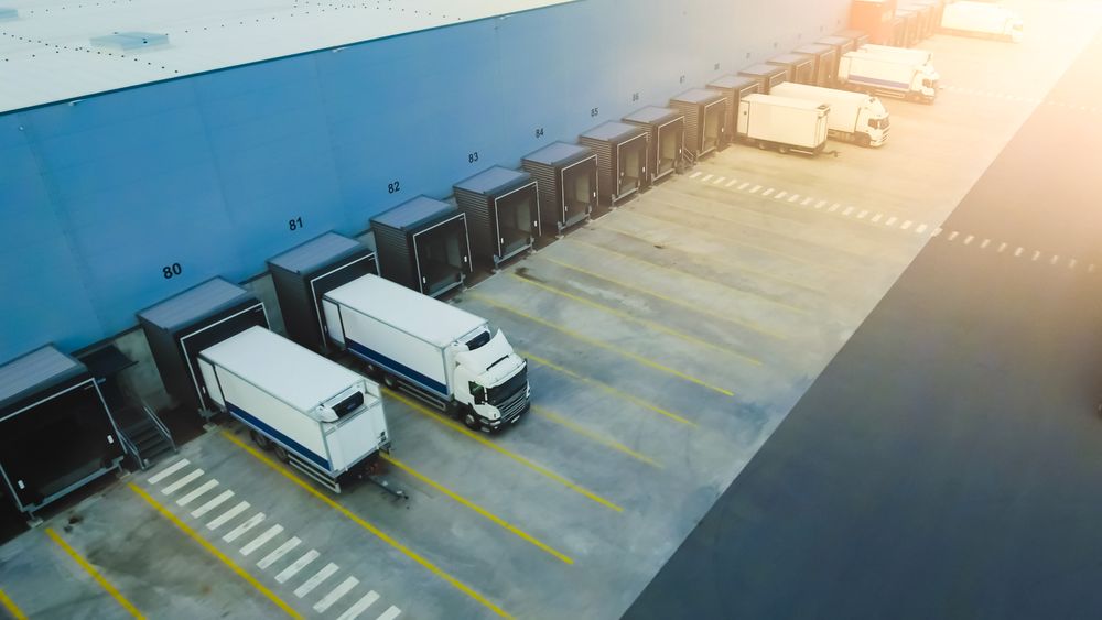 Trucks Strategically Align at a Vast Warehouse Loading Dock, Optimizing Logistics and Ensuring Seamless Cargo Handling Under the Bright Afternoon Sun