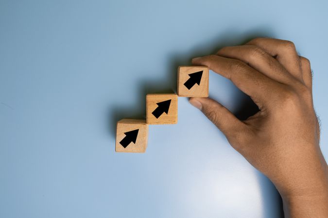 male hand put walking on arrow up stack wooden blocks isolated orange on blue background