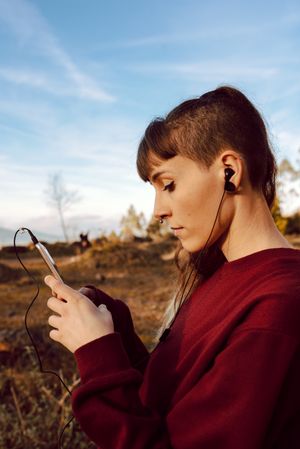 Young woman with piercing listening music on smartphone on hill