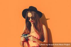 Woman wearing orange outfit and dark hat holding camera 4Brod4