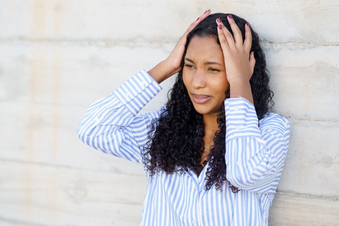A Stressed Young Woman is Holding Her Head in Discomfort Against a Wall, Struggling With Tension
