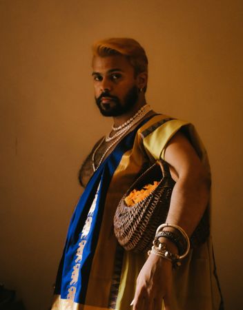 Indian man in sari holding a basket of orange flowers