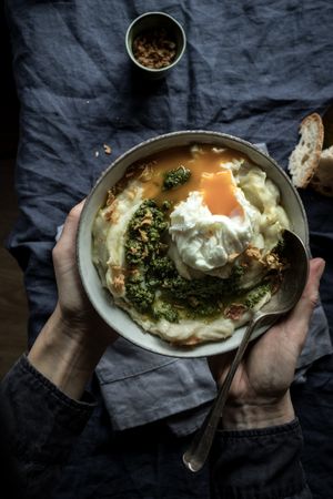 Person holding bowl with cauliflower puree with pesto and eggs