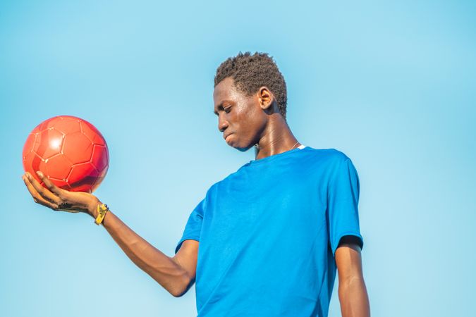 Black teenager with football ball against sky