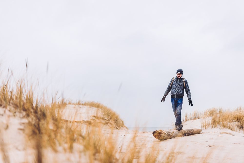 Man walking between sand field with dry grass