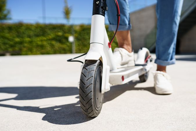 Close up of electric scooter front wheel parked in the sun with woman standing on it
