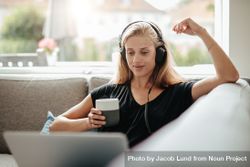 Young woman with headphones holding a cup of coffee and looking at laptop bDVOy5