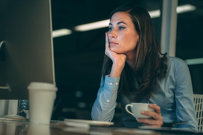 Businesswoman sitting in office looking at computer holding a coffee cup