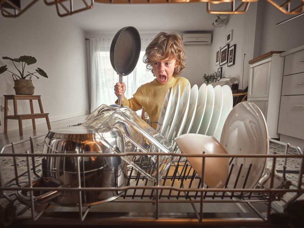 Positive boy with frying pan near dishwasher