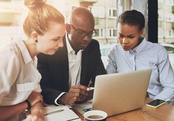 Multi-ethnic group of serious people gathered around a laptop and working