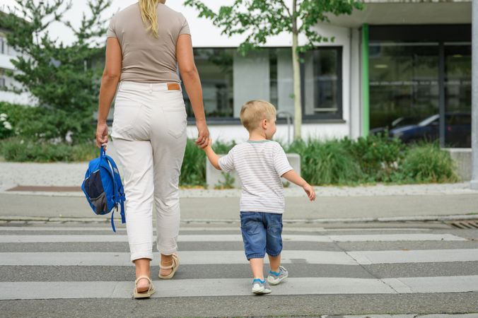 Unrecognizable mother and son crossing road on white marks