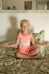 Happy girl sitting in lotus pose on bed