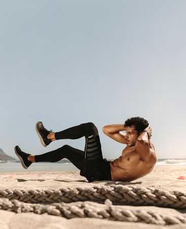Male trainer doing core workout on a beach