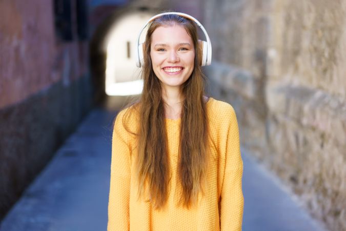 A Joyful Young Woman Wearing Headphones While Walking in a Charming Alleyway with Confidence