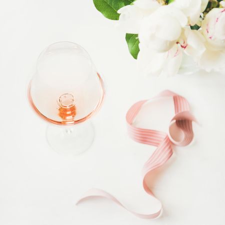 Glass of pink rose wine with flowers and ribbon, square crop