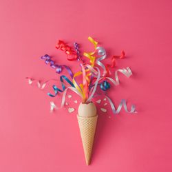 Ice cream cone with egg and party streamers on pink background