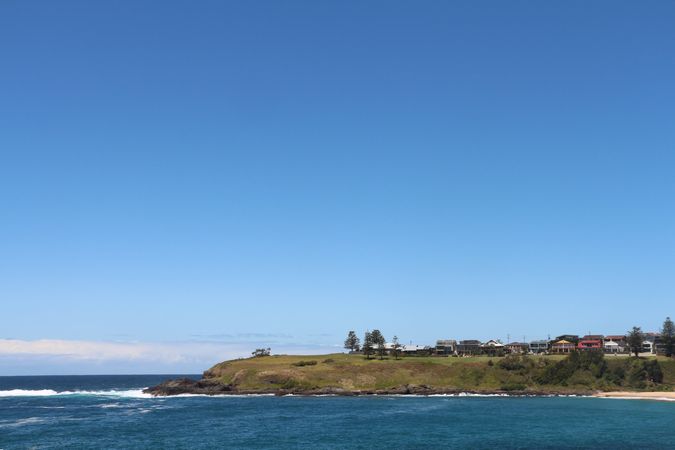 Scenic coastal view with clear blue sky and green hillside along the shoreline during daylight