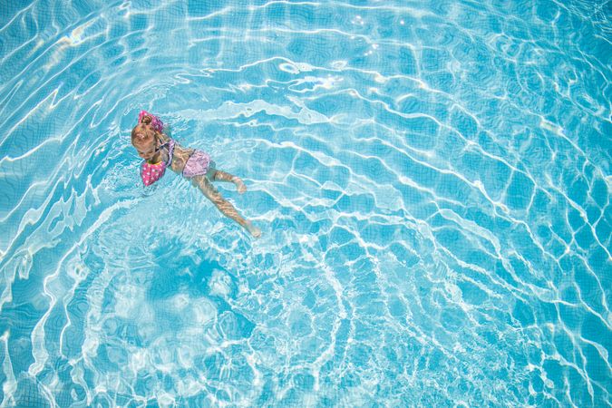 Little girl in pink bathing suit swimming in pool