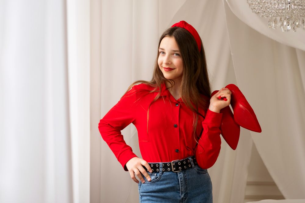 Smiling teen girl posing with red high heels indoors.