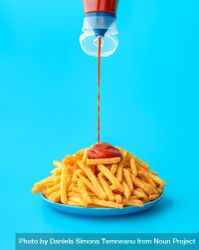 Pouring ketchup sauce over french fries, isolated on a blue background 4BWPkb