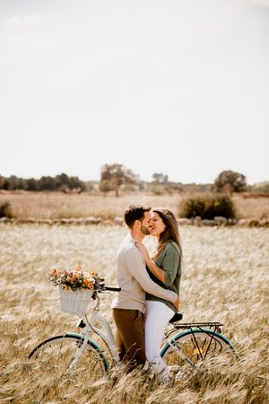 Sincere lovers posing by bicycle on rye field