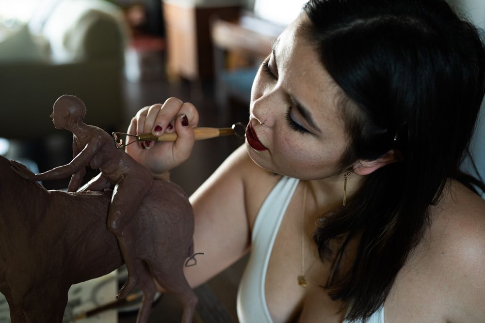 Horizontal close up of woman student shaving clay on sculpture