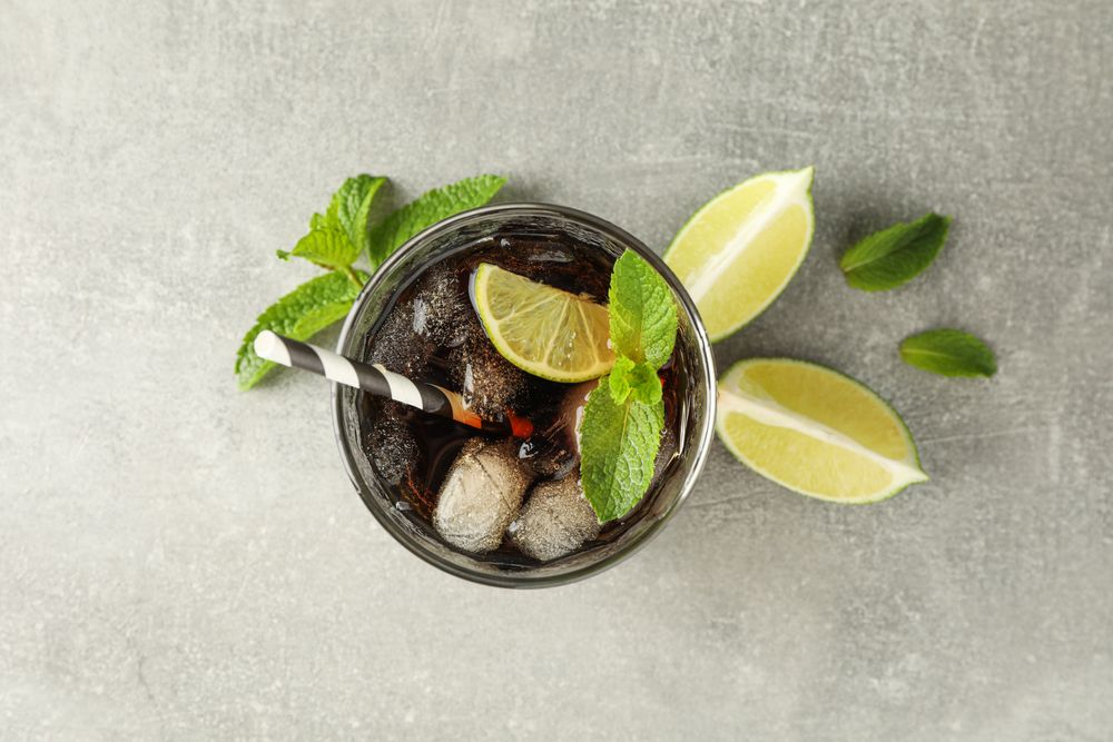 Glass with cold cola and citrus on grey table, top view