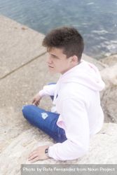 Young pensive teenager male sitting on breakwaters and looking in the distance bYqN7D