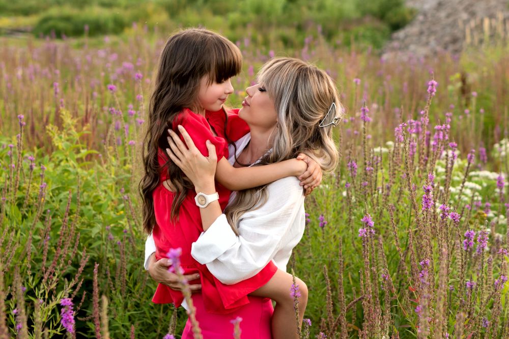 Mom and little daughter walking among meadow flowers
