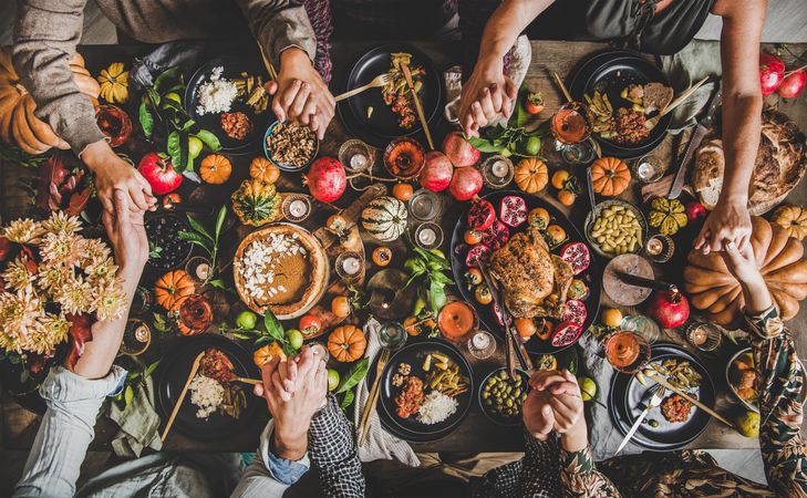 Group of people holding hands over festive table setting with roast chicken, squash, and pie