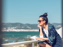 Chilling woman with book observing seascape from hotel balcony