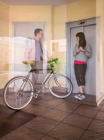 Businessman and sportive woman waving behind glass