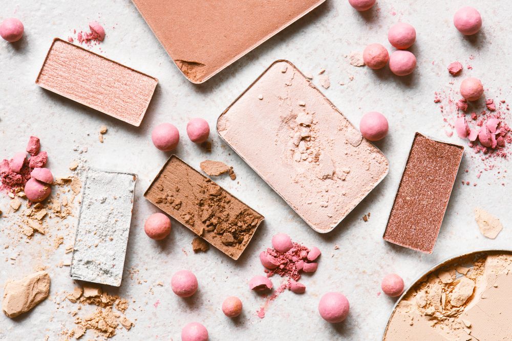 Various sizes of blushes and eyeshadows on light pink background