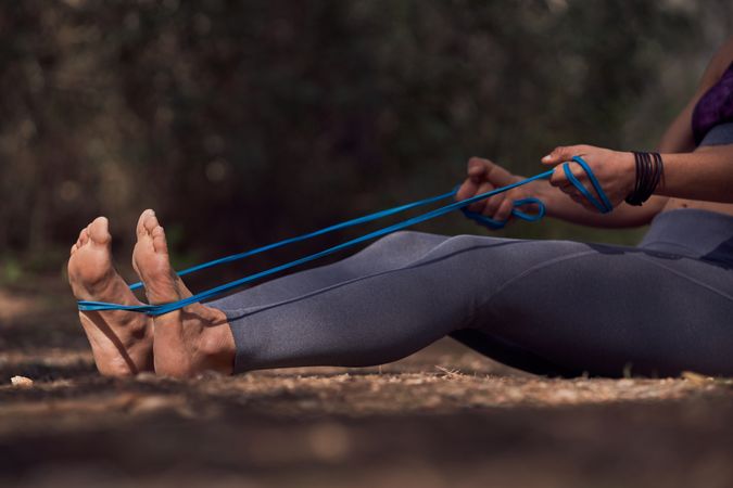 Crop sportswoman stretching legs with elastic band on ground in