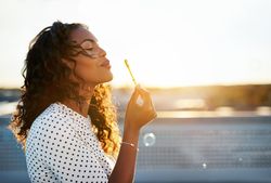 Woman pursing her lips to blow bubbles on sunny rooftop
