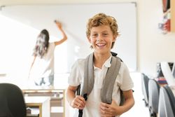 Delighted schoolboy standing in classroom with blurred teacher