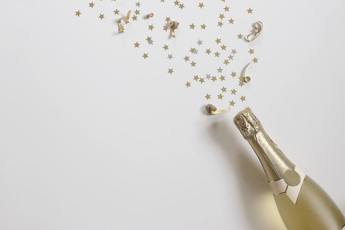 New year still life bottle of champagne and star shape golden confetti on beige table background