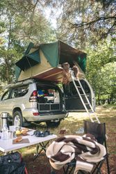Women resting lying in car tent surrounded by nature