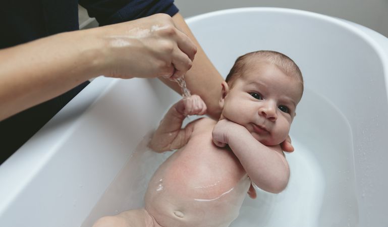 Newborn in the bathtub held by her mother