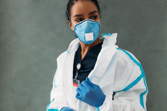 Black woman removing her hazmat suit in protective gloves and face mask