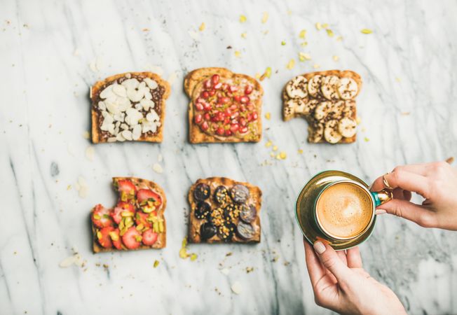 Toast topped with fresh fruit on marble background with hands lifting coffee, horizontal composition