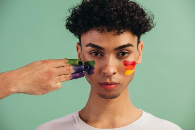 Closeup of a hand painting rainbow flag colors on man's face