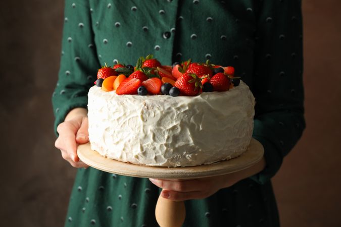 Woman holds berry cream cake against brown background. Delicious dessert