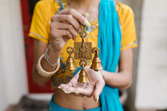 Cropped image of woman in blue and yellow sari holding three bell brass with Ganesha Hindu deity