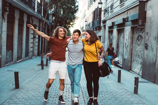 Cheerful multiracial friends hugging and walking along city street
