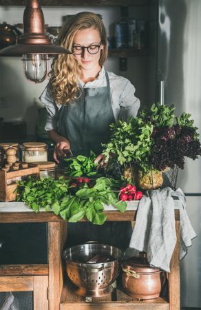 Blonde woman in glasses chopping fresh herbs in rustic kitchen